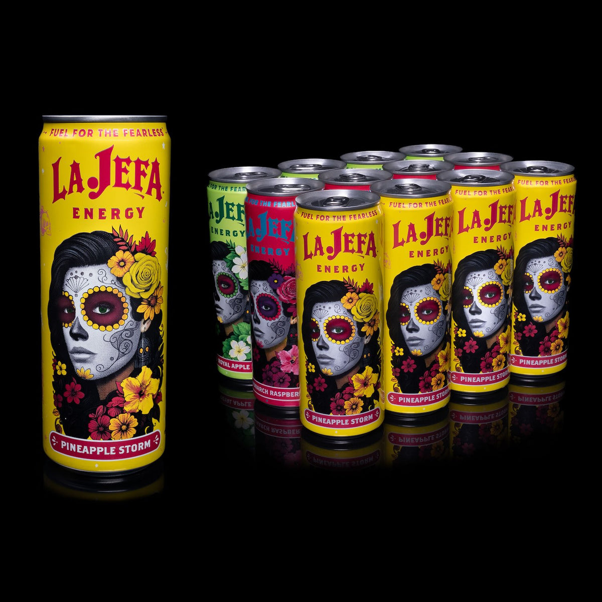 A group of La Jefa Energy beverage cans arranged on a black reflective surface, with one large yellow Pineapple Storm can in front and several smaller multicolor flavor cans behind it. The front can features a Day of the Dead style face illustration with floral details and the La Jefa branding.